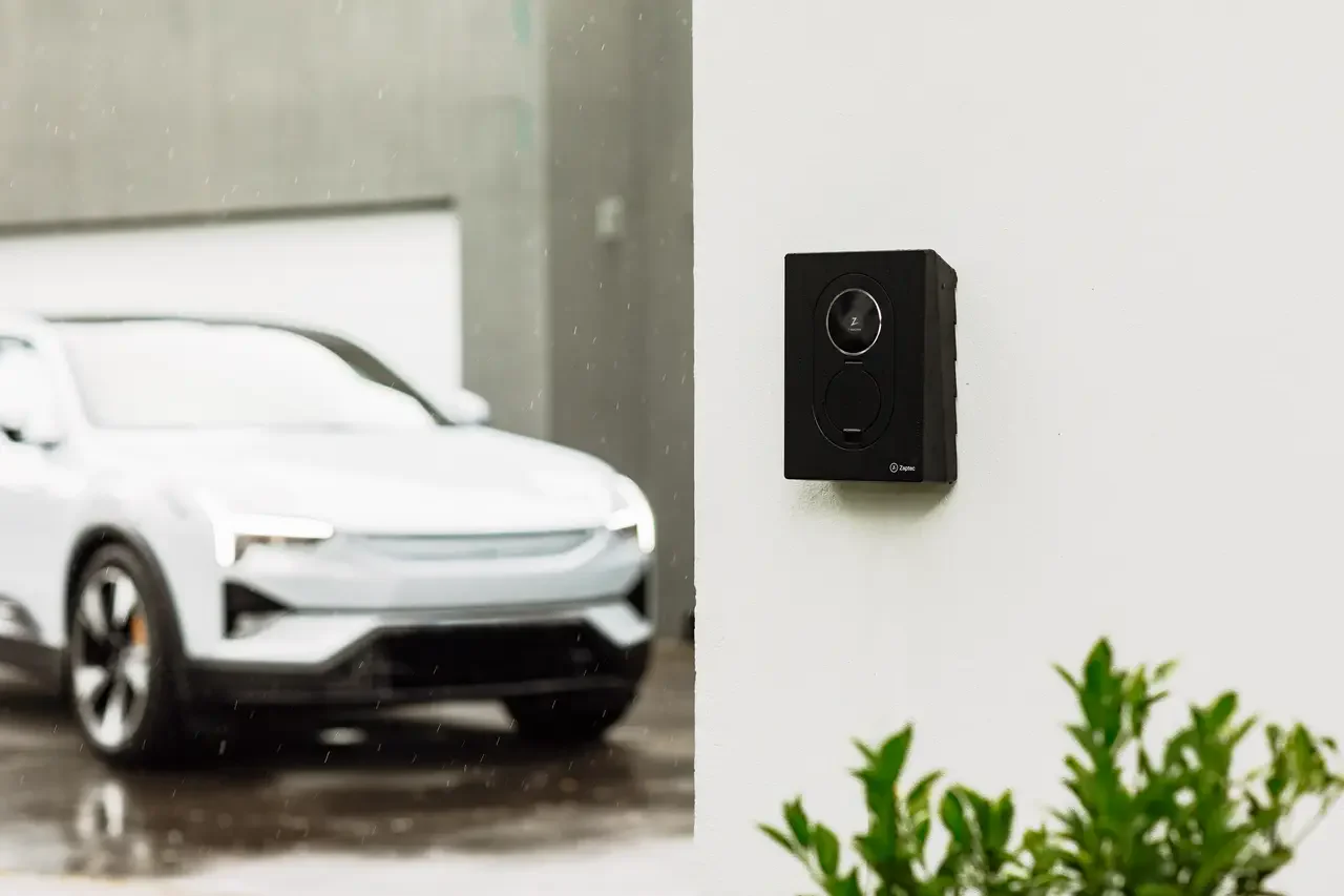 Laadpaal aan een muur met een elektrische auto op de oprit